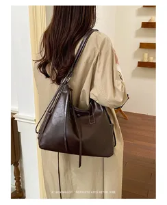 Rear view of a model carrying a brown faux leather tote with a long shoulder strap indoors