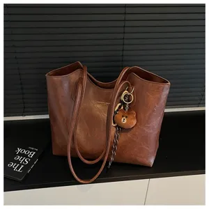 Nahaufnahme einer braunen Kunstledertasche mit langen Henkeln, Kette und kleinem Teddyanhänger