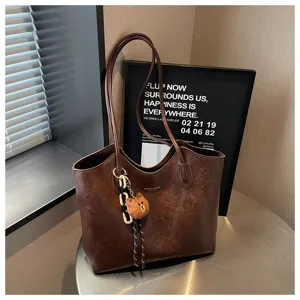 Braune Kunstledertasche mit langen Henkeln und Bärenanhänger auf einem runden Metalltisch