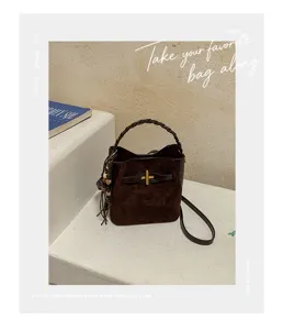 Brown suede-textured bag with a braided handle, gold clasp, dangling charm, and shoulder strap