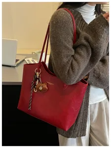 Frau trägt eine geräumige rote Tasche mit Teddyanhänger und geflochtenem Riemen im Büro