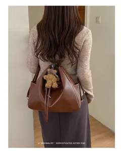Rear view of a brown faux-leather bag worn over the shoulder, with a teddy bear charm