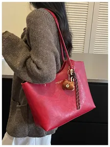 Rote Tasche über der Schulter getragen, mit plüschigem Bärenanhänger und gestreiftem Flechtband.