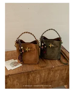 Two suede-textured bags in brown and olive, with braided handles and beaded charms on wooden table