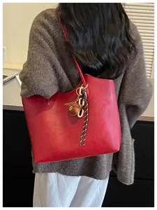 Rote Schultertasche von hinten mit Kettenakzent, Seilquaste und Plüschbären-Anhänger im Büro