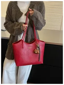 Rote glänzende Tasche am Model, mit zwei Henkeln, Teddybär-Anhänger und geflochtenem Riemen