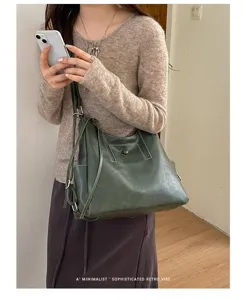 Model carrying a dark green soft leather tote with contrast stitching and adjustable shoulder strap