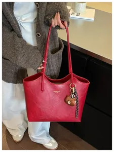 Eine Person hält eine rote Kunstledertasche mit langen Henkeln, Teddybär-Anhänger und Karoband