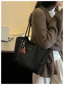 Schwarze Tasche über der Schulter, mit goldener Prägung und braunem Plüschanhänger am Arbeitsplatz