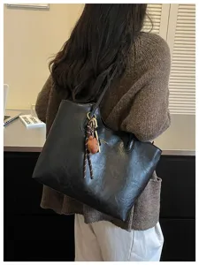 Rückansicht einer schwarzen Schultertasche mit geknitterter Oberfläche und Anhänger aus Holz.