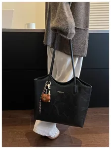 Schwarze Tasche beim Tragen, mit Plüschbären-Anhänger und dekorativer geflochtener Kette.