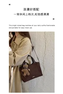 Lifestyle view of a dark brown suede tote worn over a beige coat, with a teddy bear charm