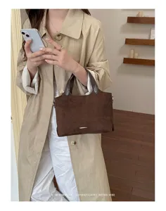 A model carries a brown suede-textured tote with dark handles and a slim metal accent