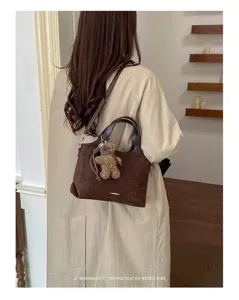 Back view of a coffee-brown suede-textured shoulder bag with a teddy bear charm and silver trim
