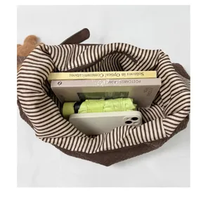 Vue de dessus d’un sac tressé brun à doublure rayée, avec livres, parapluie et téléphone