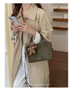 Lifestyle view of an olive-green suede-look bag with brown handles and a teddy bear charm