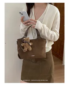 Brown suede-look tote with a plush bear charm, carried with a cream knit cardigan and corduroy skirt.
