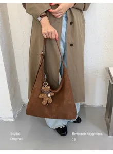 Modèle portant un sac marron à texture tressée, avec un petit ours en peluche, devant un mur clair