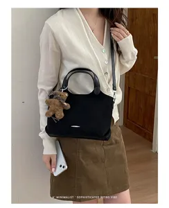 A model wears a black suede-look handbag with a shoulder strap and brown teddy bear charm