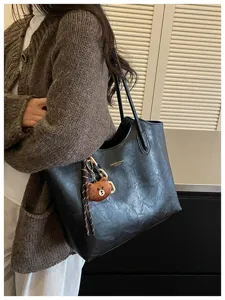 Alltagsaufnahme einer getragenen schwarzen Tasche mit strukturierter Oberfläche und Teddybär-Anhänger