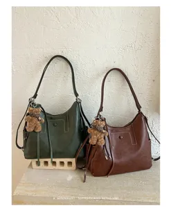 Two leather-look bucket bags in dark green and brown, with teddy charms and plaid scarf accents