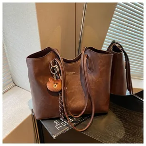 Braune Kunstledertasche mit langen Trageriemen und kleinem Teddybär-Anhänger auf einem Tisch