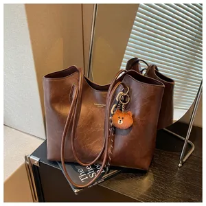 Detail der braunen Kunstledertasche mit Falten, Teddyanhänger und buntem Webband