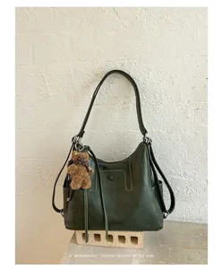 Green faux-leather bag with stitched panels, round snap and brown teddy charm on a display stand