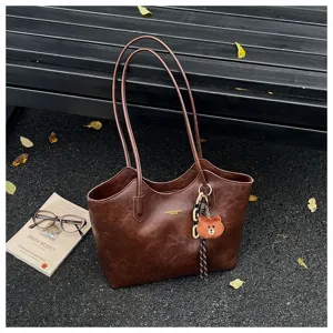 Braune Kunstledertasche mit langen Henkeln und Bärenanhänger neben Büchern und Brille