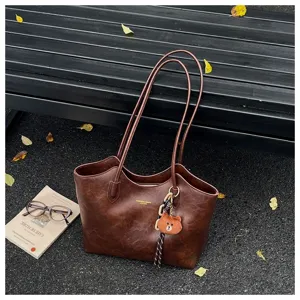 Braune Tasche mit Used-Look aus Kunstleder, langen Henkeln und kleinem Bärenanhänger im Freien