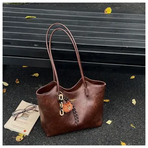 Braune Kunstledertasche mit langen Henkeln und Bärenanhänger auf einer Bank im Freien