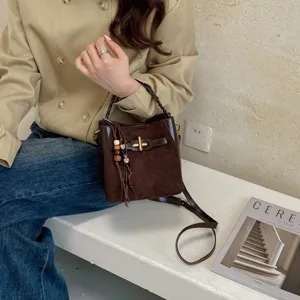 Brown faux suede bucket bag with gold buckle and beaded charm, shown with a shoulder strap
