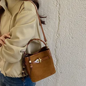 Brown faux suede bucket bag with braided handle, gold-tone buckle and crossbody strap, worn by model