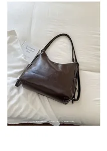 Dark brown leather-look bag on white bedding, with a softly creased finish and adjustable strap