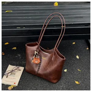 Braune Kunstledertasche mit langen Henkeln und Bärenanhänger neben Buch und Brille