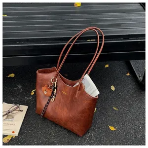 Braune Kunstledertasche mit doppelten Schulterriemen und Bärenanhänger, draußen neben Büchern