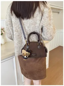 Vue de dos d’une femme portant un sac brun effet daim avec un pendentif chat en peluche