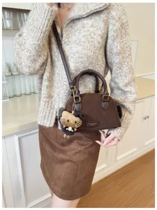 Petit sac brun effet daim avec breloque ourson en peluche, porté devant un comptoir de cuisine