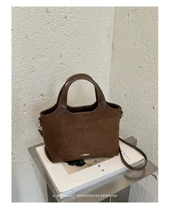 Brown suede-look handbag with top handles and a detachable shoulder strap on a display surface