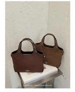 Two brown suede-look tote bags with dark handles displayed side by side on a shelf beside books