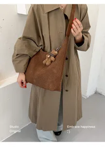 Vue en situation d’un sac bandoulière tissé marron avec un pendentif ourson porté sur un manteau