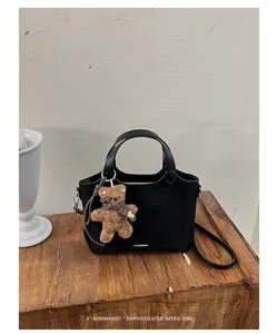 Black velvet-look bag with a brown teddy charm, displayed on a wooden table against a pale wall