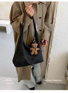 Une personne tient un sac noir tressé à longue bandoulière, orné d'un petit pendentif ours brun