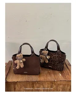 Two brown suede tote bags, one leopard print, with teddy bear charms displayed on a wooden table
