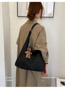 Vue de dos avec sac noir tressé, bandoulière réglable et breloque ours en peluche.