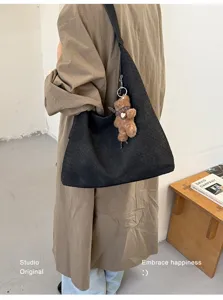 Sac noir à texture tressée porté à l’épaule avec un petit ours brun, dans un intérieur neutre