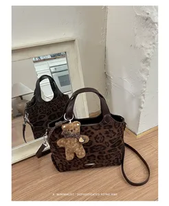 Brown leopard-print bag with leather handles and a teddy bear charm, displayed beside a mirror