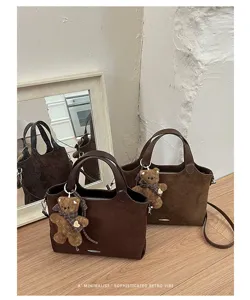 Two brown suede-look bags with teddy bear charms and shoulder straps displayed on a wooden table