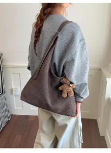 Vue de dos d’un sac brun à texture tressée, porté à l’épaule avec un petit ours en peluche