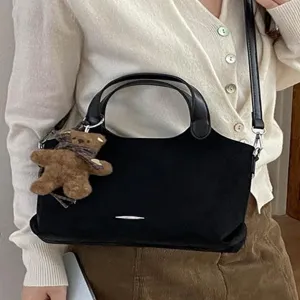 Black suede tote handbag with leather handles, shoulder strap and teddy bear charm, worn crossbody